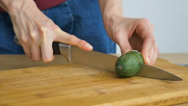 Female hands is cutting a fresh green feijoa fruit on a cut wooden board. Exotic fruits, healthy eating concept