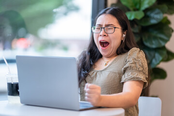 asian of freelance business female wearing wireless earphones bored yawning in front of casual working with laptop computer and coffee and smartphone in coffee shop like the background