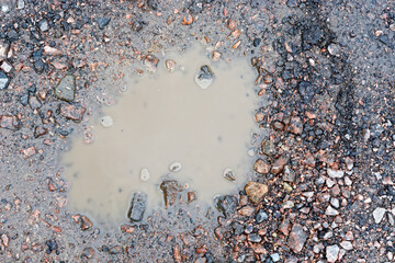 Top view of a small puddle of muddy water on a rocky country road.