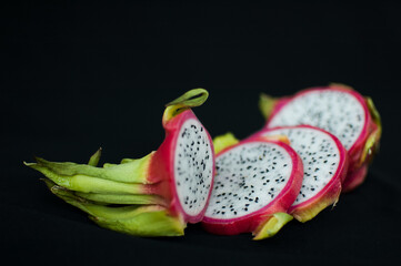 Slices of dragon fruit or pitaya with pink skin and white pulp with seeds on black background....