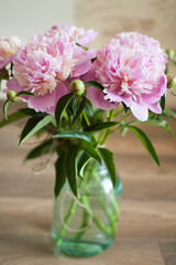 Bouquet of fresh pink peonies in transparent jar standing on the table indoors