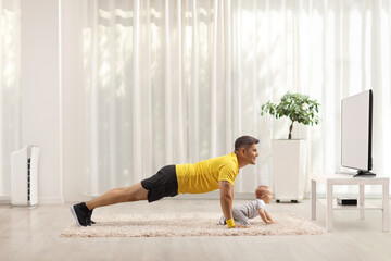 Father exercising in front of tv and baby crawling on carpet