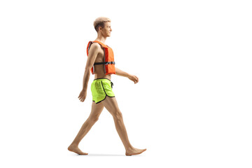 Full length profile shot of a guy in swimming shorts and life vest walking