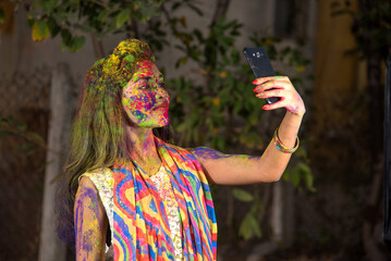 Young girl with colorful face taking selfie using smartphone on Holi festival. Festival and technology concept