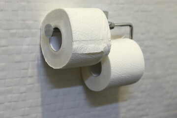 Two rolls of toilet paper on a white tile background