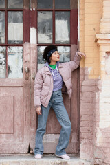 Fototapeta na wymiar African american woman in jacket standing near old building