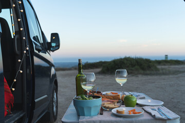 Camping table with wine and food next to van facing the sea
