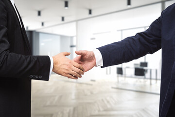 Two businessmen shake hands on the background of modern furnished office, partnership concept,...