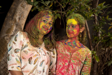 Portrait of happy young girls having fun with colorful powder at Holi festival of colors