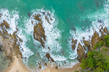 Aerial top view of white waves in green sea hit on the large rocks in summer day. .Beach sea space area. green sea, waves crashing on the rocks.. At Kalim Beach Phuket Thailand.