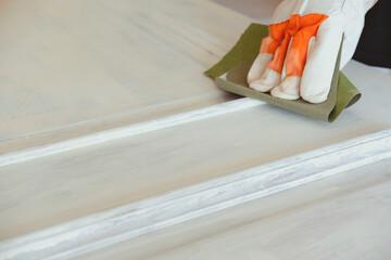 Close-up of a hand with sandpaper on a white door. Homemade concept. House renovation concept.