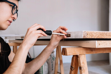 Close-up of a young Caucasian woman attaching a hinge to a door with a screwdriver. Homemade concept. Home renovation concept.