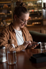 vertical portrait of smiling young woman using mobile phone for chatting or texting in backery and coffe shop
