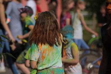 Child stained with paint hair head clothes.Dirty kids painted in different colors.Lots of little boys and girls school children at the dry paint festival outside in summer.Vacation concept