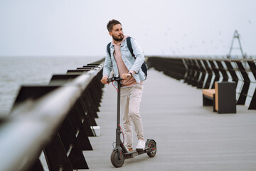 Young man riding electric scooter on a pier near the sea. Ecological transportation concept.