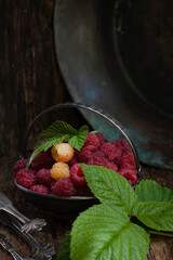Raspberries in silver bowl with green raspberry leaf on wooden table, low key, selective focus, vertical, copy space