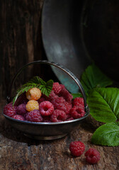 Raspberries in silver bowl with green raspberry leaf on wooden table, low key, selective focus, vertical, copy space