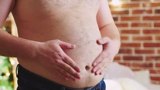 Man slaps beer belly with his hand. Men use big belly as a drum. Obese man slaps stomach his hands. Adult human with curvy physique clap hands on stomach. Concept of body positive