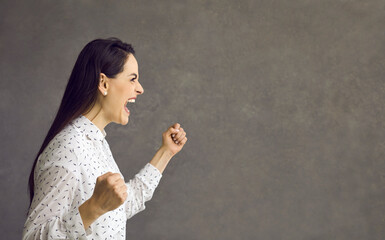Angry young caucasian woman with clenched fist screaming showing furious face side view studio...