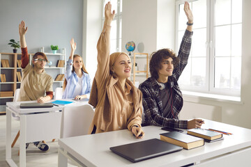 Highschool or college diverse teenager student group raising hands answering question studying sitting at desk in classroom on lecture. Education, getting knowledge and learning at school lesson