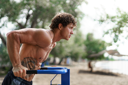 Fit Man Workout Out Arms On Dips Horizontal Bars Training Triceps And Biceps Doing Push Ups. Handsome Man Doing Exercise On Parallel Bars. Male Athlete Exercises On Parallel Bars Outdoor