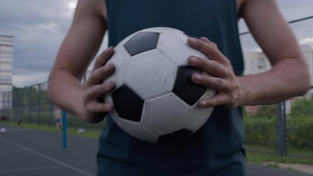 Young caucasian amateur man practicing soccer skills and tricks with the football ball at sunset in an playground. The guy spinning the ball on his finger. 4K UHD slow motion RAW graded footage
