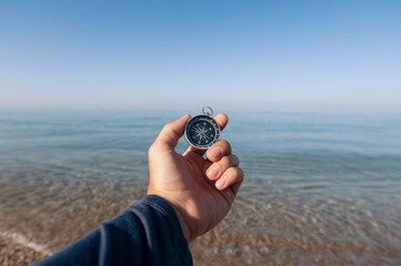 The traveler is looking for direction with a compass on the coastline of the morning sea. A man's hand holds a magnetic compass. © yanik88
