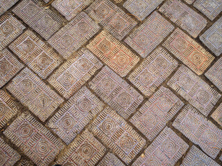 Old worn decorative brick pavers with intricate carved design. Medium close view.