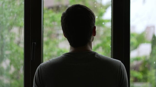Silhouette of a man looks outside the window at the rain