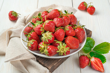 Ripe red strawberries in a white plate on a light background.