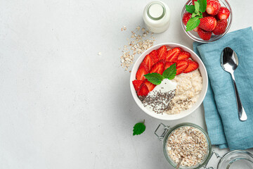 Healthy oatmeal porridge with strawberries, chia seeds and yogurt on a gray background with space to copy.