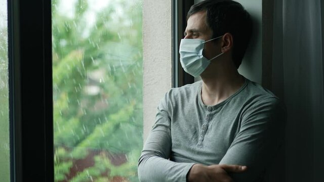 Man on self-isolation in a mask looks out the window