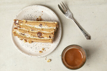 Slice of napoleon cake, glass cup of espresso coffee and a dessert silver fork on a creamy clay...