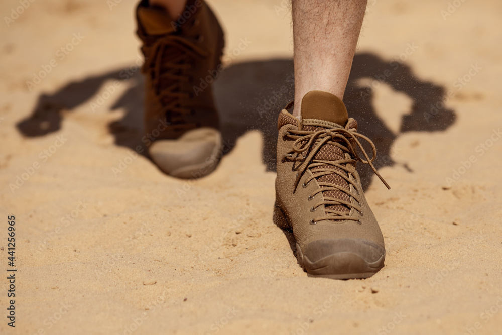 Wall mural Close up of man legs walking in tactical shoes on sand surface