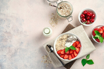 Oatmeal porridge with fresh berries and chia seeds on a light pink background with ingredients.