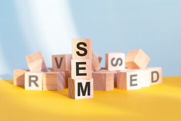 wooden cubes with letters sem arranged in a vertical pyramid, yellow background, reflection from the surface of the table, business concept