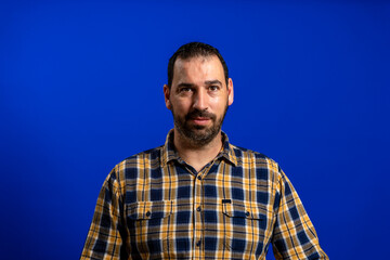 Portrait of handsome bearded man in a yellow plaid shirt isolated on blue studio background