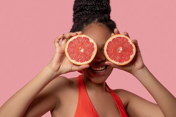 Dark-skinned woman holding grapefruit slices and looking happy