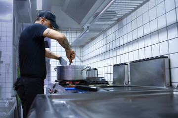 Young chef prepares grilled vegetables on cast iron griddle in his restaurant. Healthy food preparation concept.