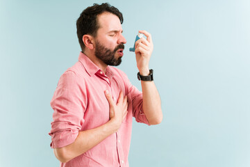 Sick man using an inhaler during an asthma attack - obrazy, fototapety, plakaty