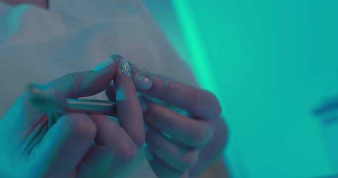 The close-up multiloop edgewise arch wire is holding in the hand of a female orthodontist and by using dental forceps is clenching and bending it.