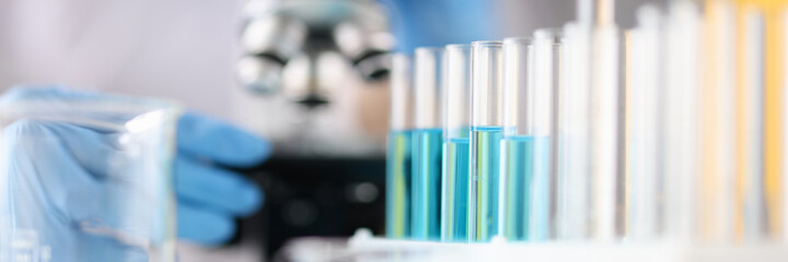 Test tubes with blue liquid standing against background of microscope closeup