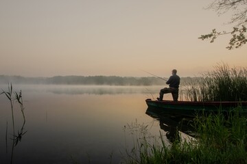 Naklejka na ściany i meble fisherman during foggy summer sunrise