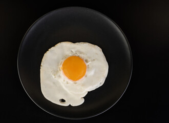 Fried egg lies on a black plate on a black background