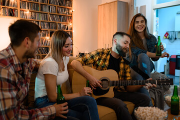 Friends on a house party having fun and drinking beer while playing guitar