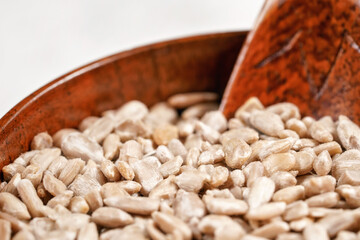 Peeled sunflower seeds in small wooden cup with little scoop, placed on white stone like board, closeup detail