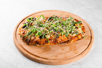 Vegan pinsa romana with mushrooms, asparagus, corn, peas, carrots, cheese and sauce, garnished with microgreens on wooden board.