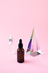 Serum jars with pipette mockups and glass pyramid prism on pink background with copy space,...