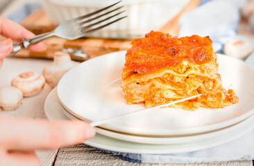 woman eating a delicious lasagna with cheese crust on a white plate viewed close up on the side showing the layers
