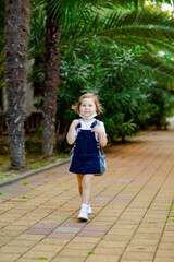 Fototapeta premium a little girl, a schoolgirl, goes to school on the street with a denim backpack, and in a medical mask